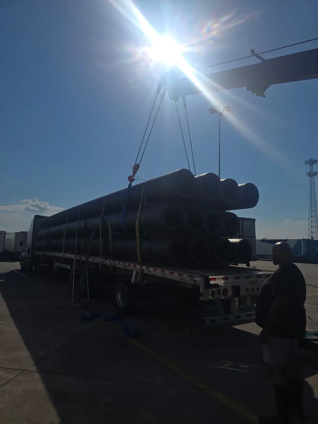 Bundles of large black pipe strapped on a flatbed trailer with rigging attached
