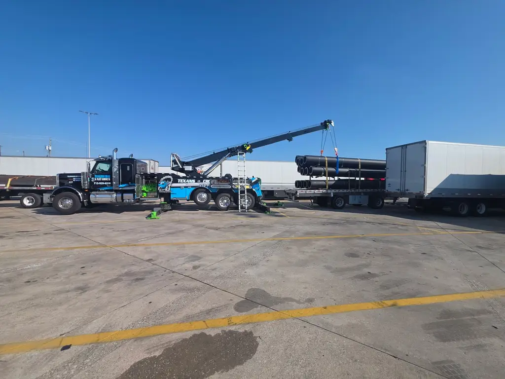 Rotator working beside a flatbed loaded with pipe and a dry van trailer