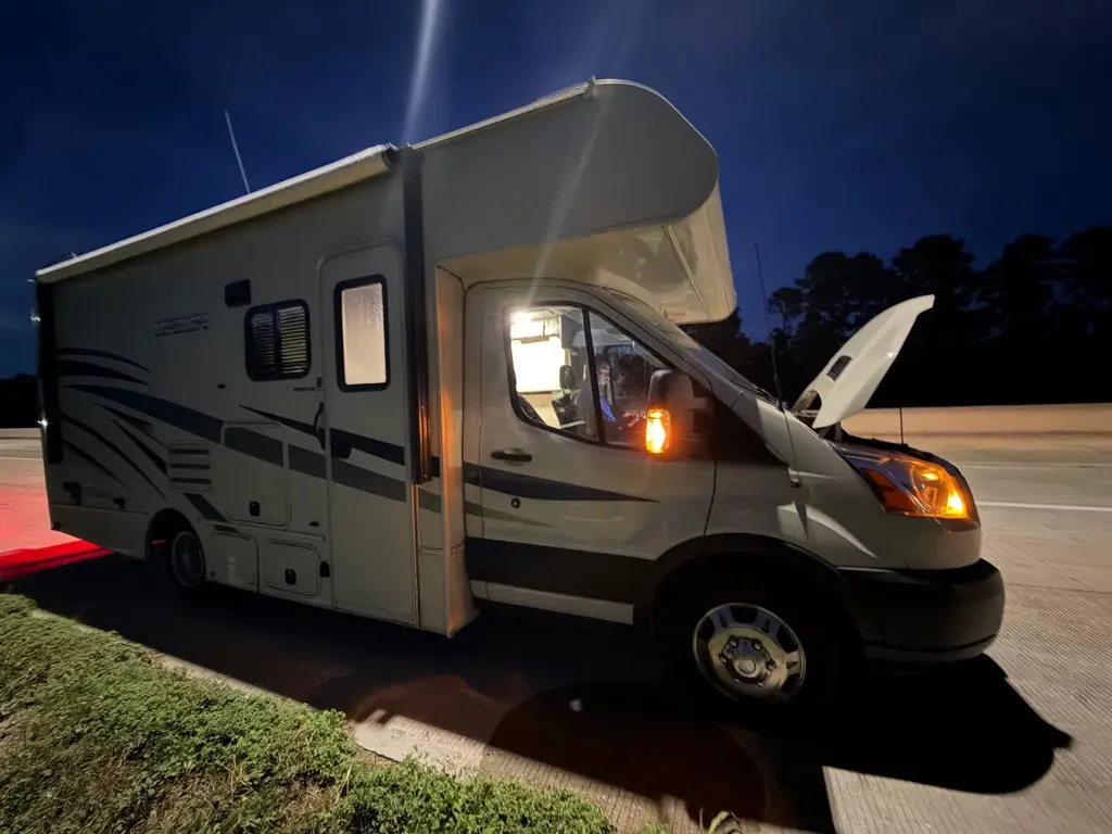 Class C motorhome on the shoulder at night with hazard lights on